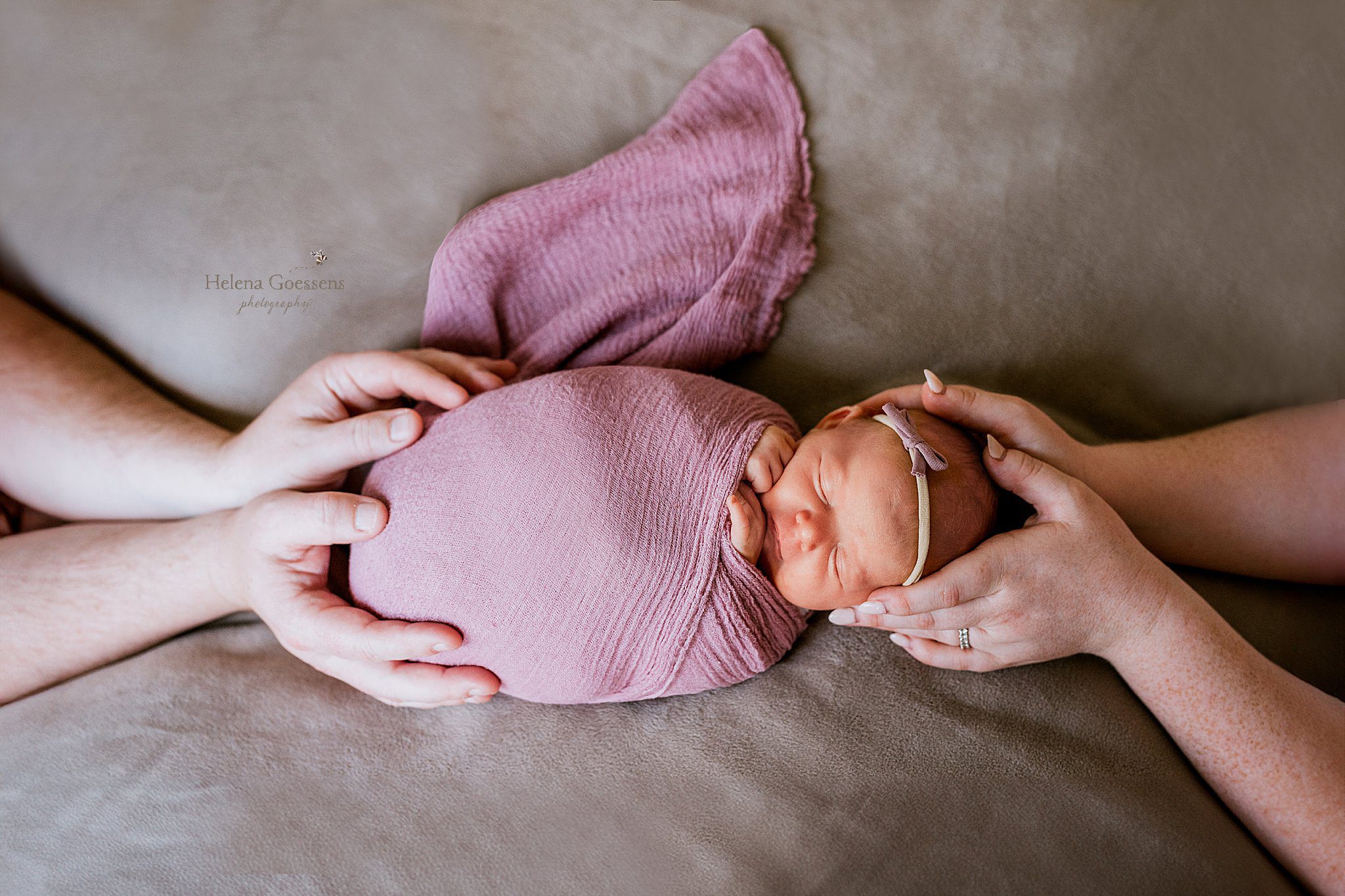 baby lays in purple wrap with mom and dad holding her head and bottom 