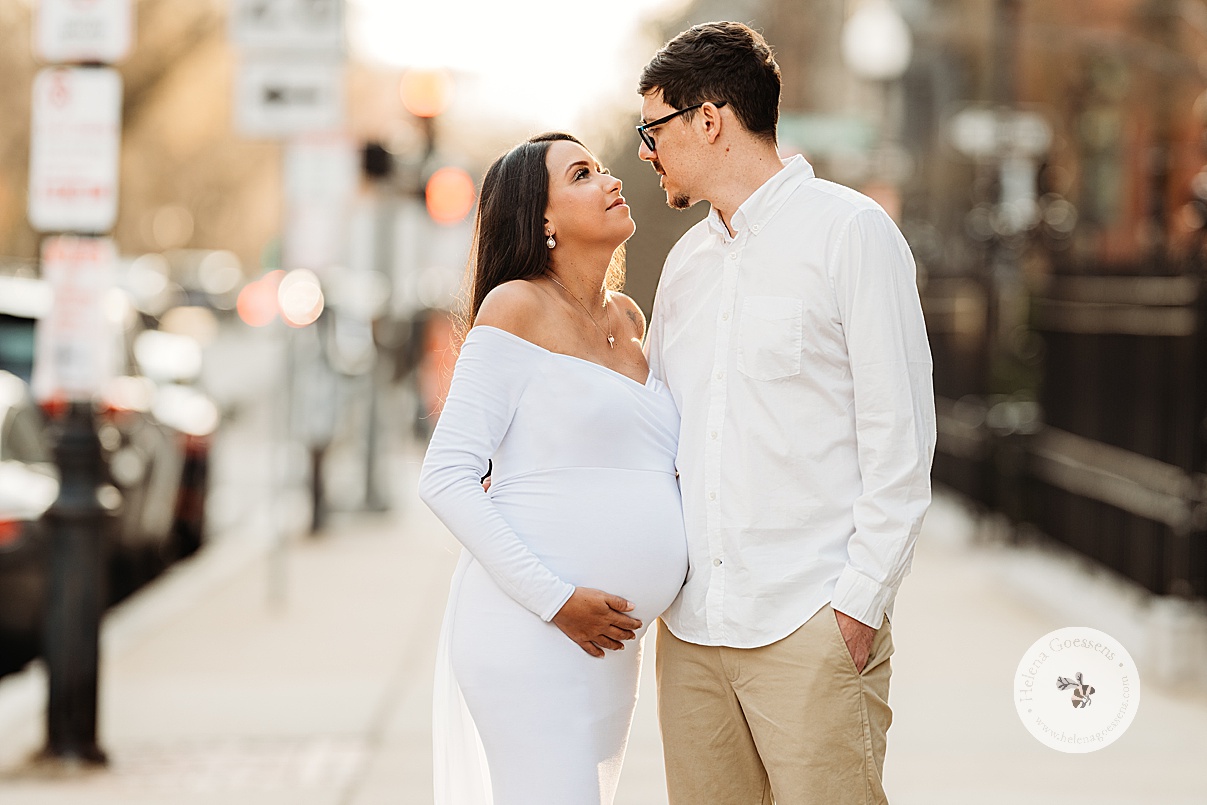 woman in white gown holds baby bump smiling at husband on street in Boston MA