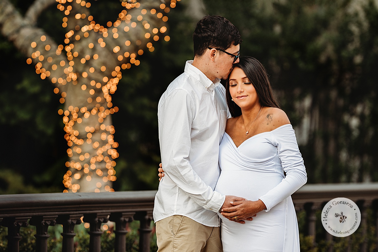woman in white maternity gown holds husband's hands to her belly during Boston Back Bay maternity portraits