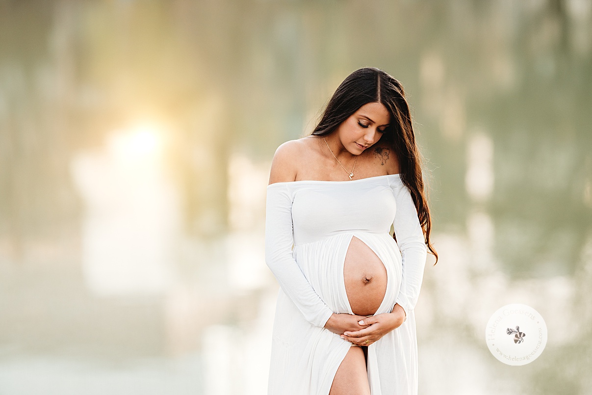 woman looks down at baby bump in white dress during Boston Back Bay maternity portraits