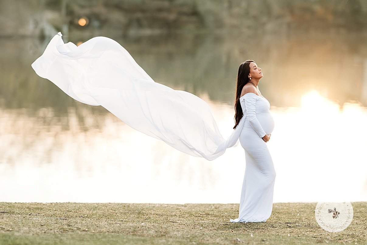 mom holds baby bump with cape floating behind her in Boston Public Garden during maternity portraits 