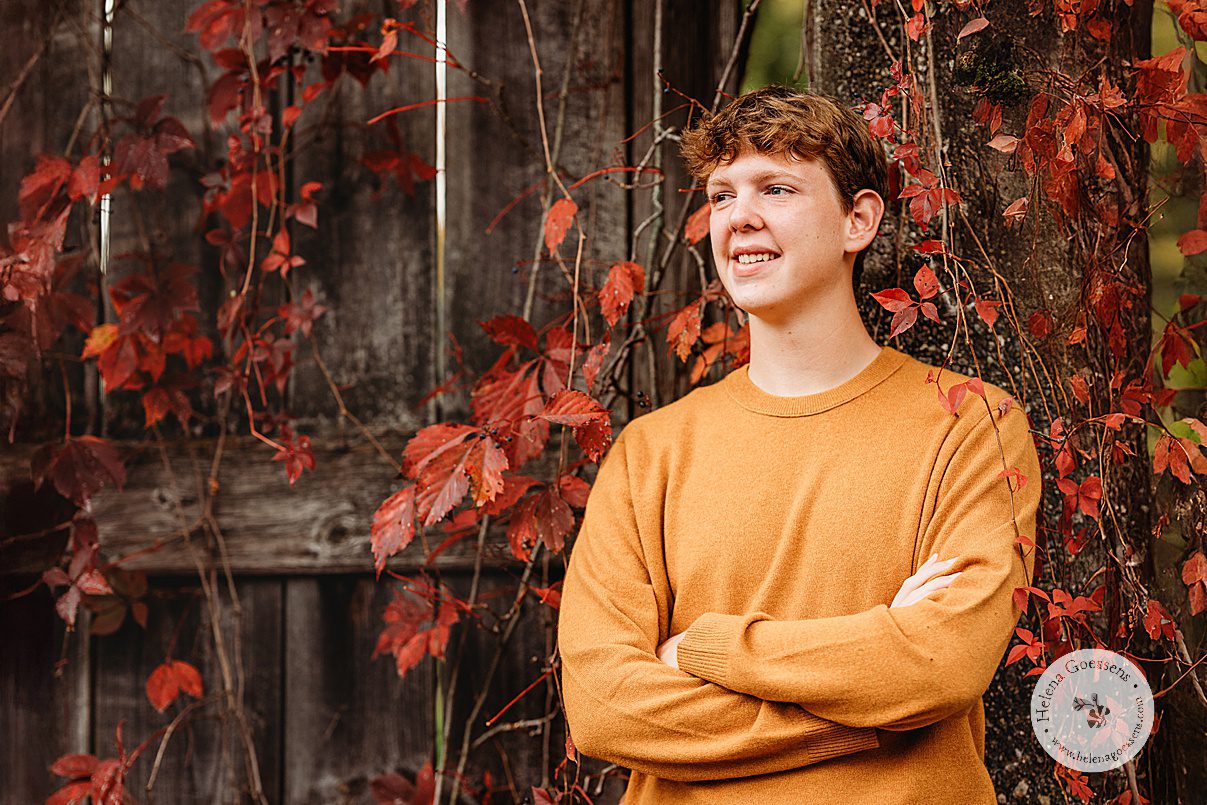 high school senior crosses arm standing in red leaves at Larz Anderson Park