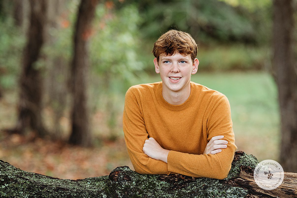 senior guy leans on fallen tree during Larz Anderson Park senior portraits