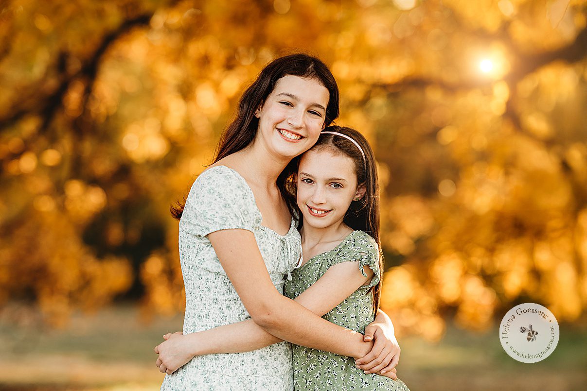 sisters in green and white dresses hug during family photos at Larz Anderson Park