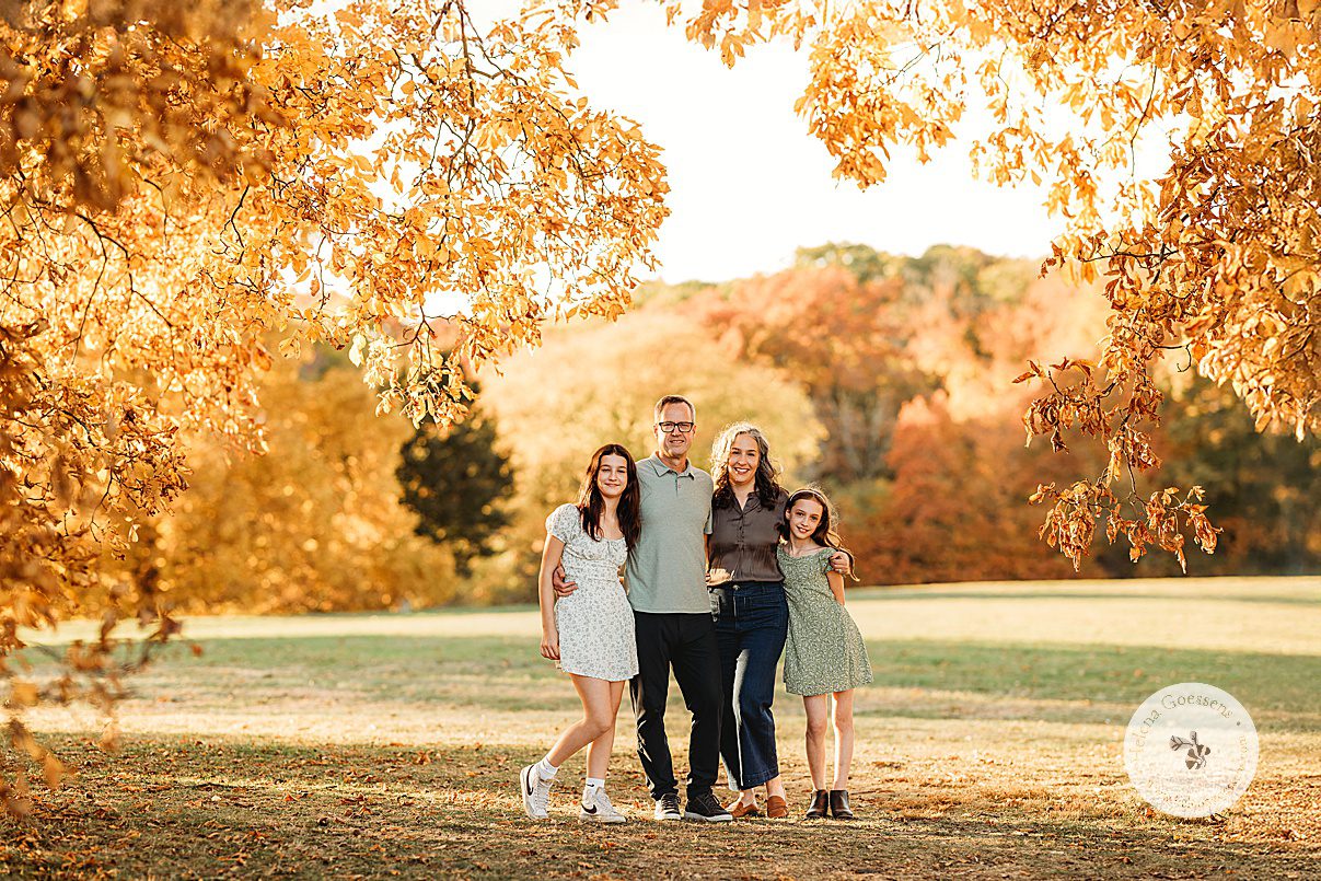 family of four hugs standing in park during family portraits at Larz Anderson Park