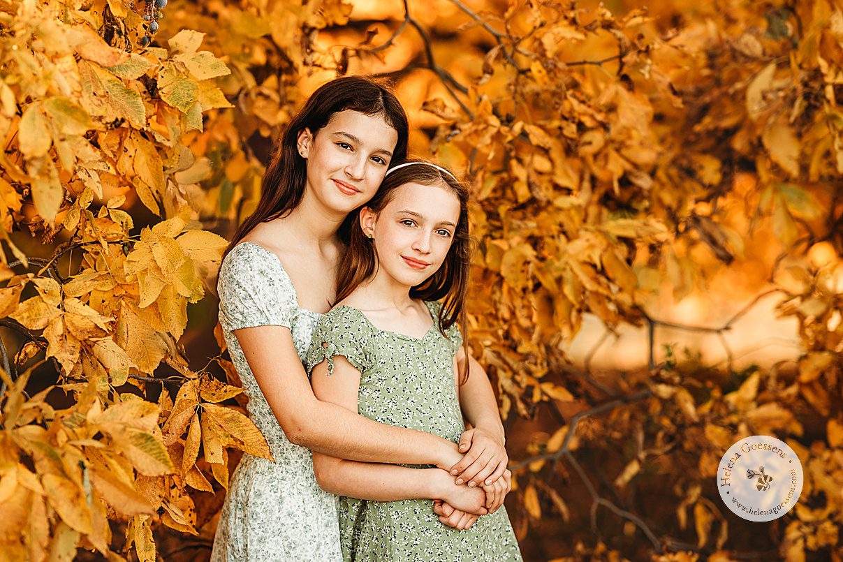 big sister hugs little sister in front of her during family portraits at Larz Anderson Park