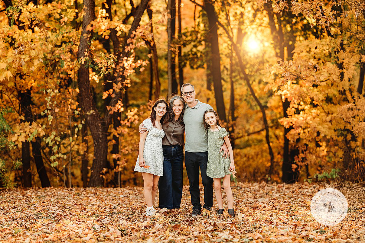 family of four hugs in front of treelike with sunset behind them during family portraits at Larz Anderson Park
