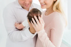 A couple smiles while holding a newborn. The woman gently holds the baby's head, and the man supports the baby's body.