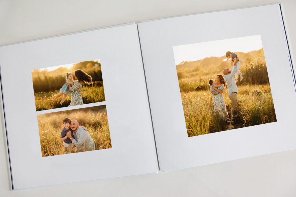 An open photo album displays family photos in a sunlit field: a woman playing with a child, a man and boy smiling, and a family of four together in tall grass—perfect moments captured as Family Photography Packages Explained.