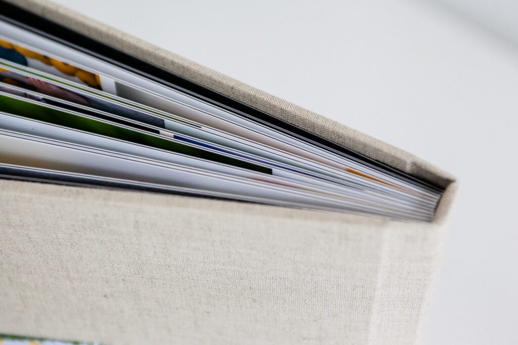 Close up of the corner of an open photo album with a beige fabric cover, featuring thick, glossy pages and colorful images—a perfect example to showcase Family Photography Packages Explained.