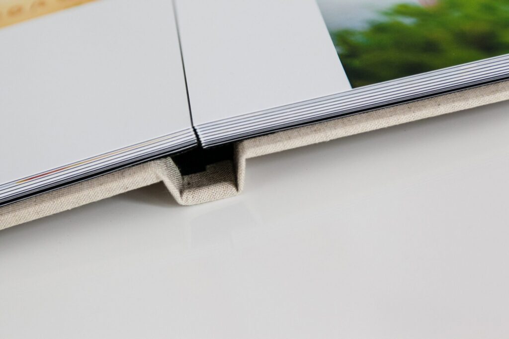 Close up of a photo book lying open on a white surface, showing thick, glossy pages and a fabric covered hardcover spine with a small notch—perfect for showcasing memories from our Family Photography Packages Explained.